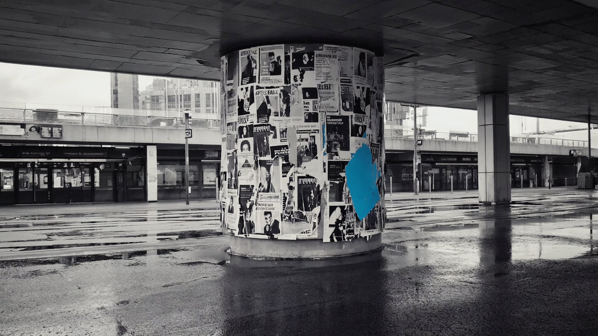 Überklebte Berliner Plakatwand mit Schichten zerrissener Konzertplakate und einem kobaltblauen Farbfleck am Rand.